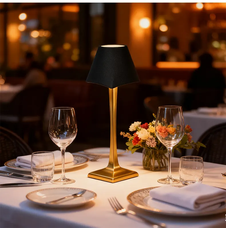 Black-shade table lamp with a gold-colored stem on a restaurant table set with glasses, plates and flowers